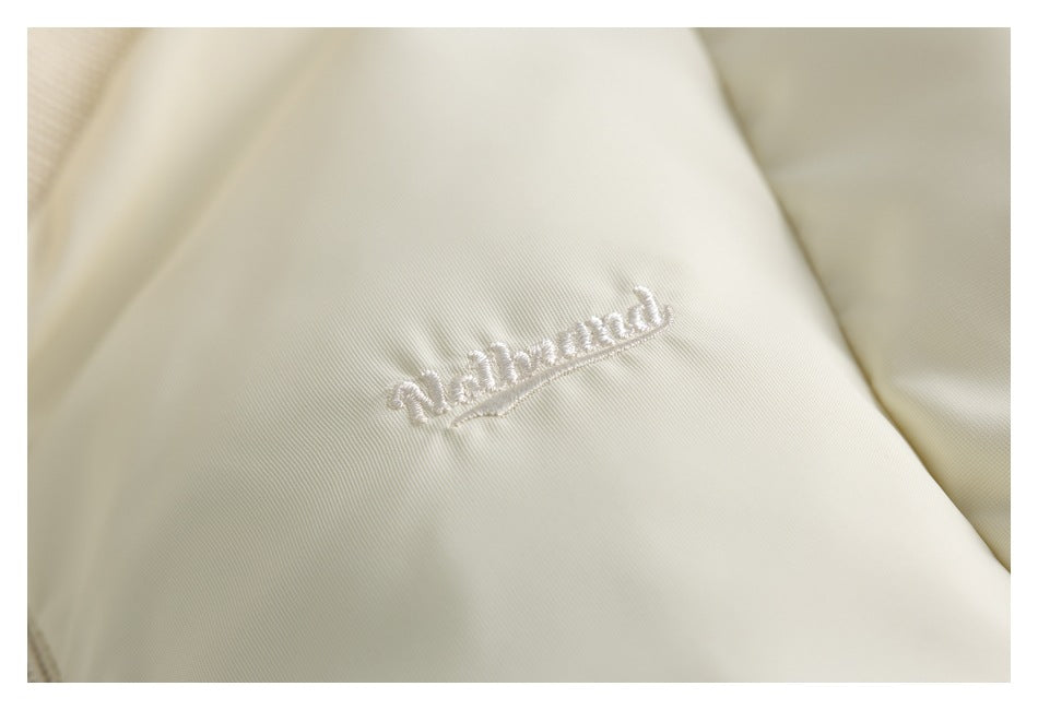 Close-up of white cursive embroidery on pale cream garment fabric.