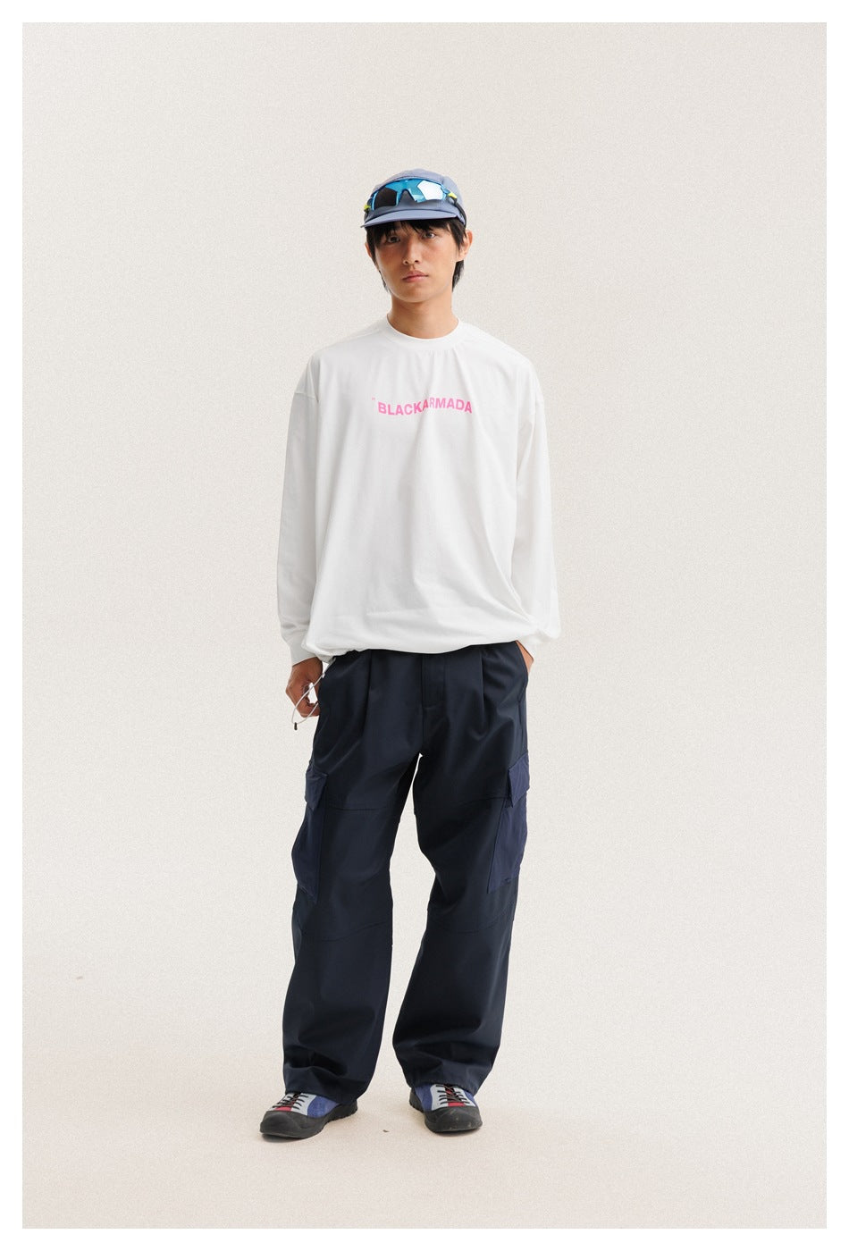 Full-length front view of a model wearing a white long-sleeve shirt with pink text and navy cargo pants.