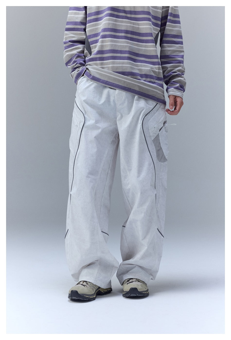 Front view of a model wearing loose light gray cargo pants with dark piping and a striped shirt.