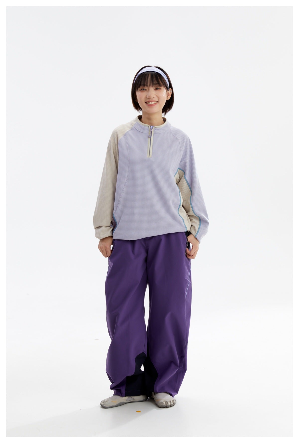 Front view of a model wearing a light lavender quarter-zip top with beige sleeves and loose purple pants.