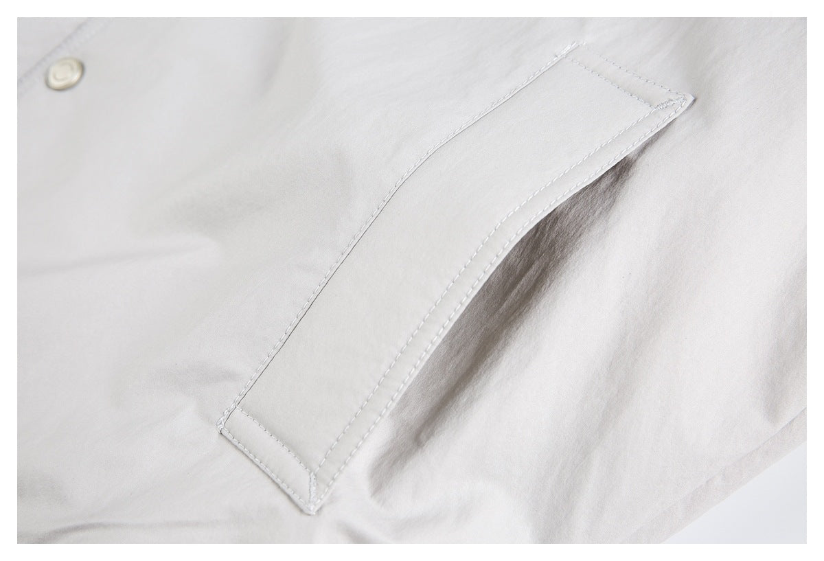Close-up of a rectangular stitched pocket on pale gray fabric, with a metal snap partly visible nearby.