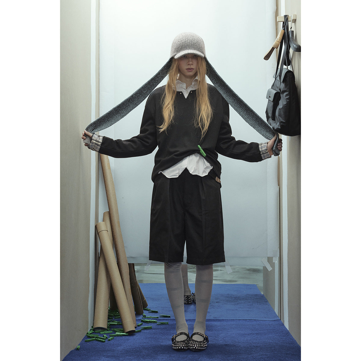 Model wearing a black pullover with plaid cuffs, black knee-length shorts, gray knit hat and tights.