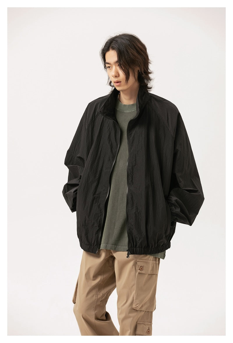 Model wearing a black zip-front jacket with a raised collar and elastic hem, styled with a gray-green top and tan cargo