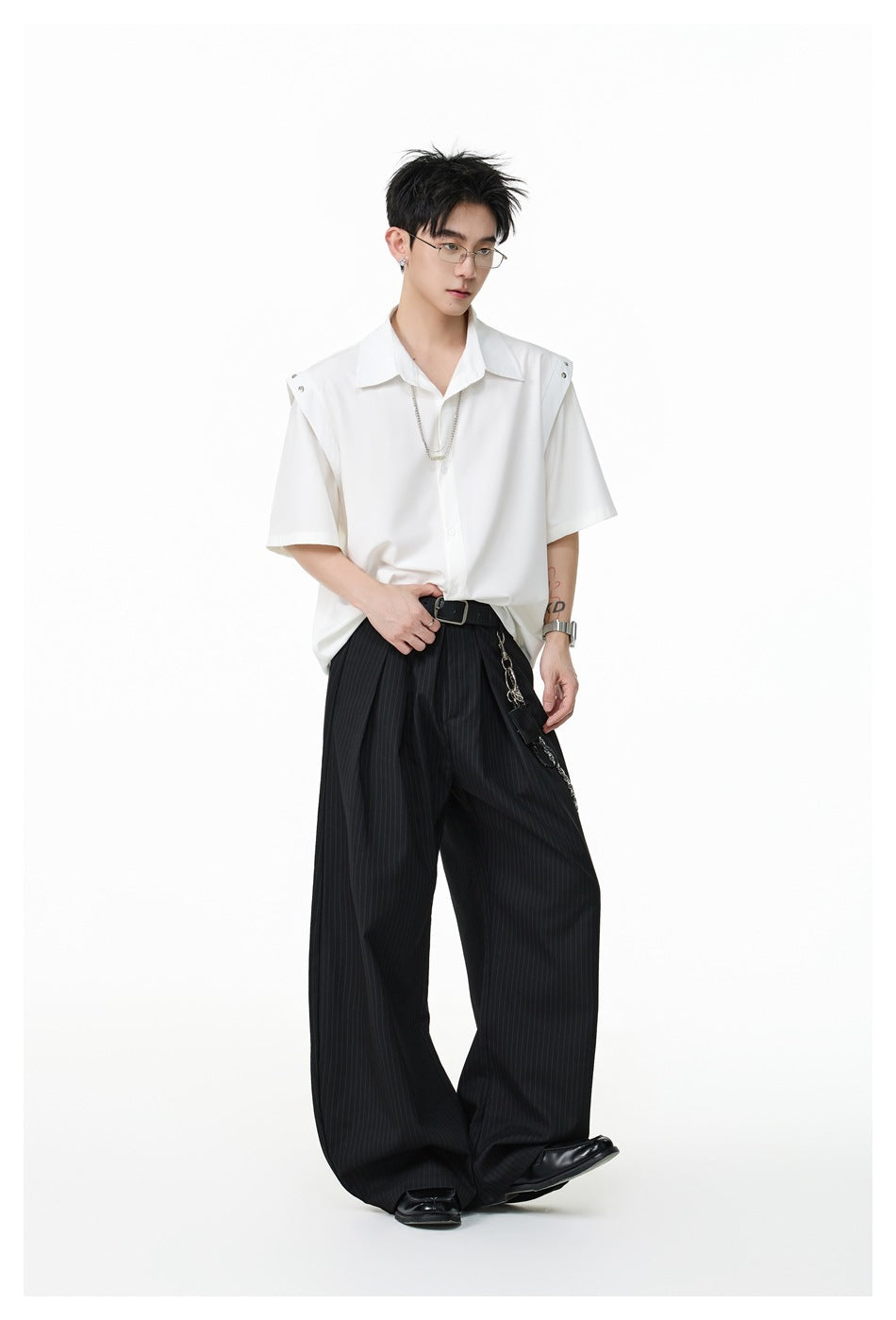Model wearing a white short-sleeve shirt with shoulder studs and a chain, styled with wide pinstripe black trousers