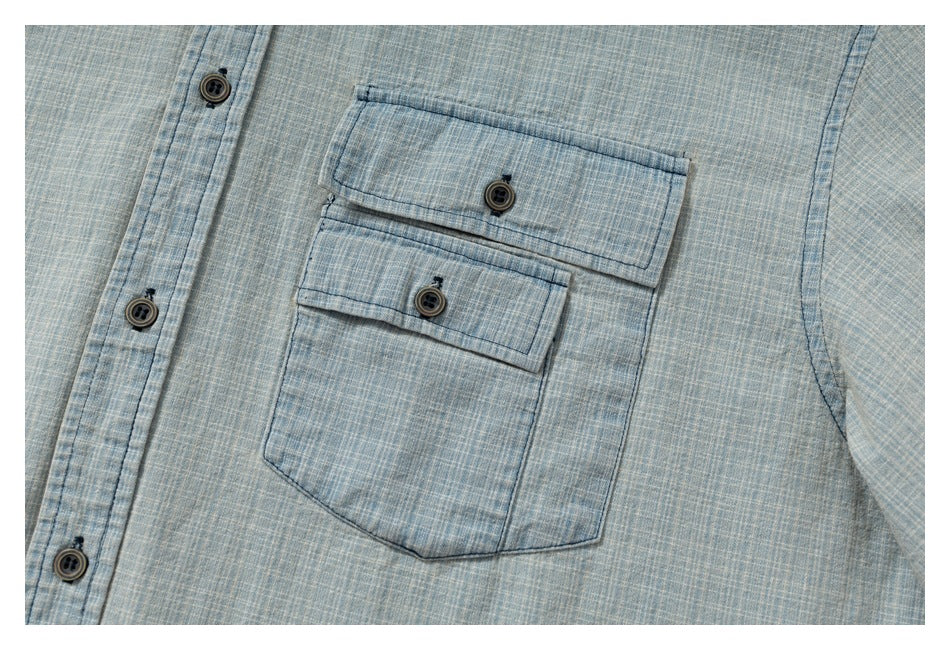 Close-up of the light blue crosshatch shirt's chest pocket with two buttoned flaps.