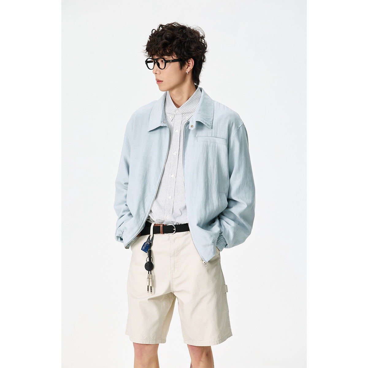 Model wearing a pale blue zip-front jacket over a checked shirt and cream shorts.