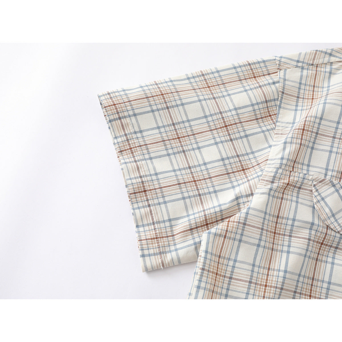 Close-up of a short sleeve and seam on a cream shirt with blue-gray and rust plaid.