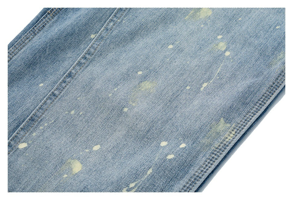 Close-up of light blue denim with scattered pale distressed marks and a visible seam.