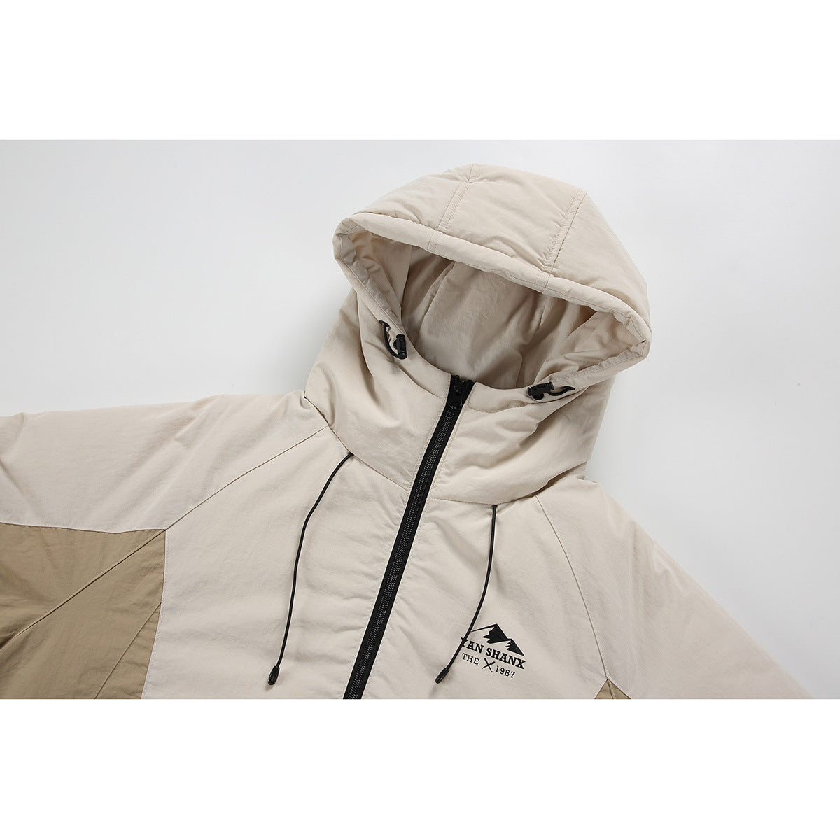 Close-up of a cream hooded jacket with black drawcords, zipper, and a small printed chest logo.