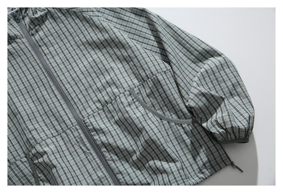 Angled close view of the gray-green plaid jacket front, showing the zipper, one curved pocket, and an elastic cuff.