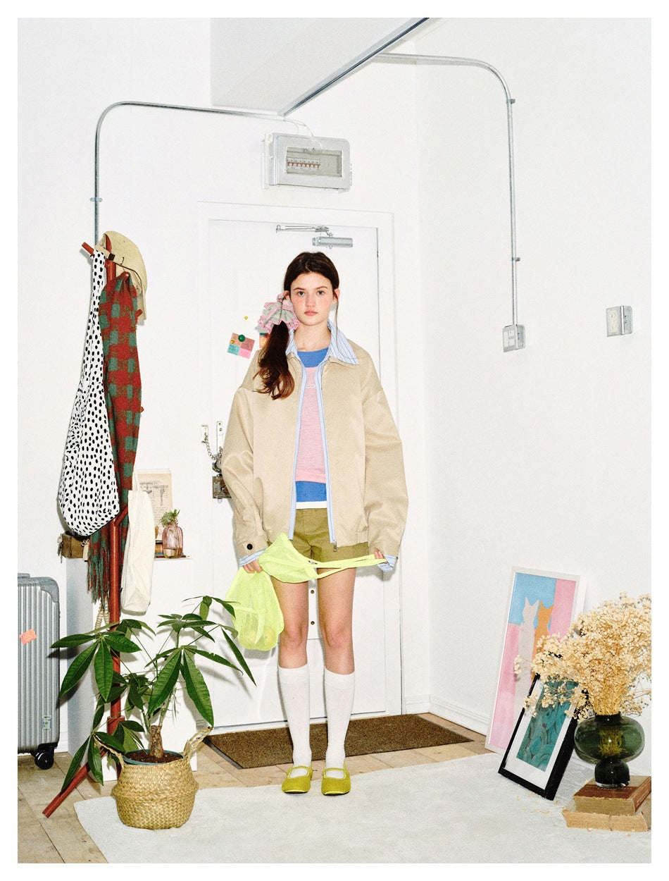 Full-length model wearing a beige zip jacket with blue striped trim, olive shorts, and white knee-high socks.