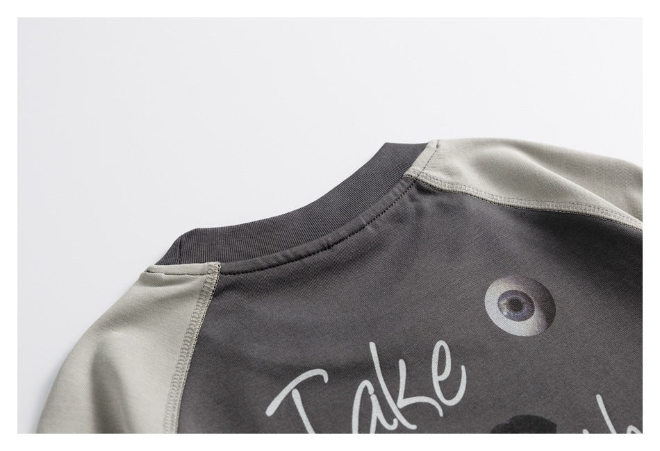 Close-up of a charcoal top with light gray raglan sleeves, ribbed neckline and part of a printed graphic.