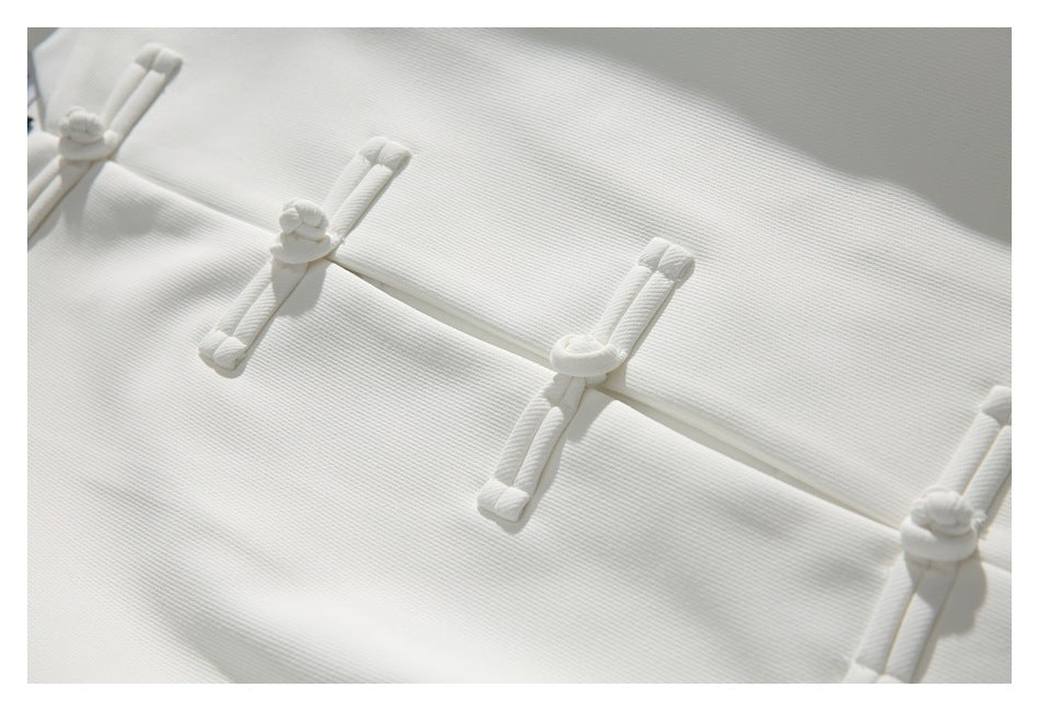 Close-up of the white jacket's knotted frog closures and fine textured surface.