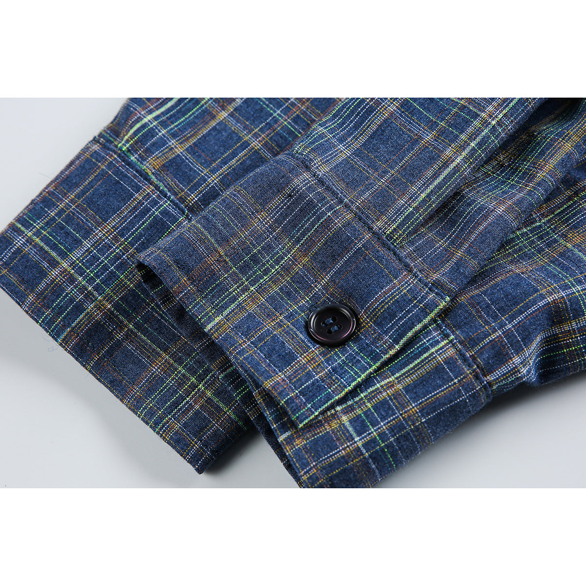 Close-up of a blue plaid shirt cuff with a black button and folded fabric.
