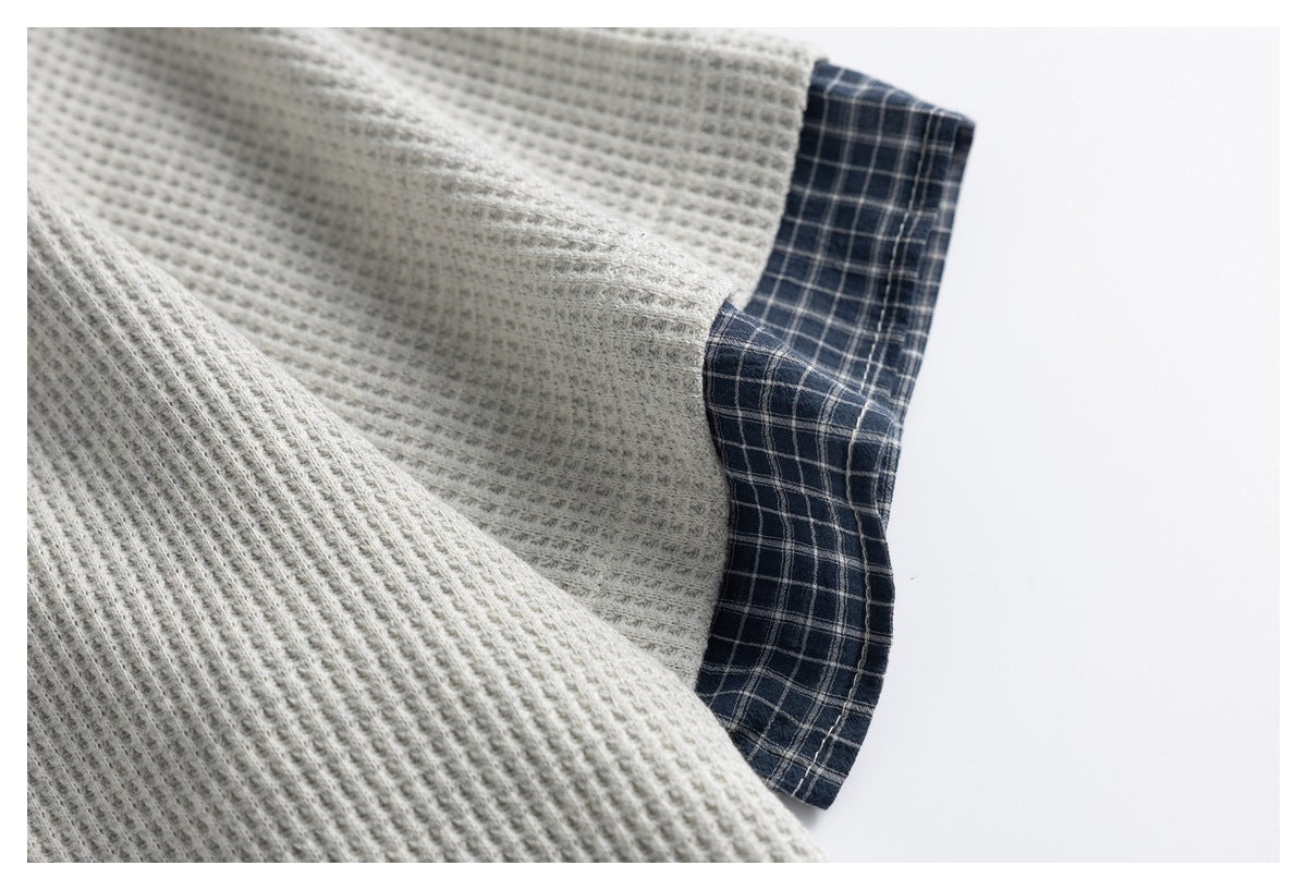 Close-up of light gray ribbed knit fabric beside a navy plaid garment edge.