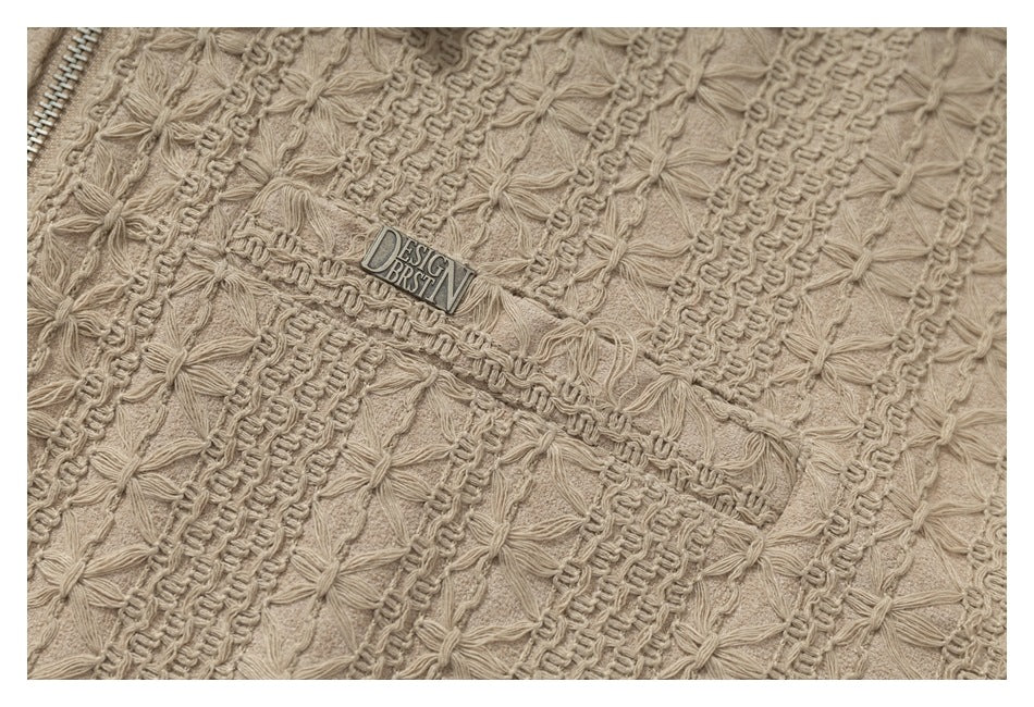 Close-up of beige textured fabric with raised floral stitching, ribbed bands, a zipper edge and a small metal label.