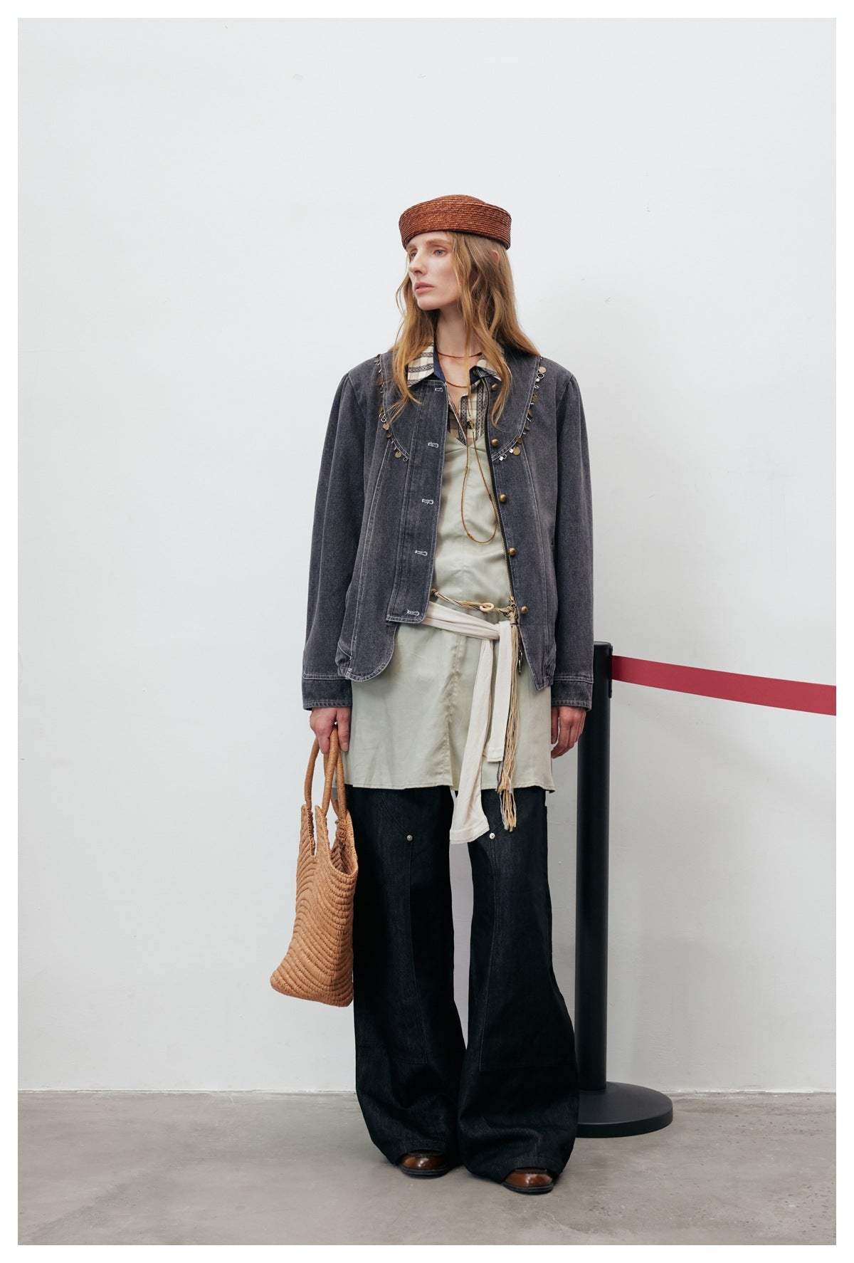 Model wearing the gray denim jacket open over a pale green dress with wide-leg dark pants, hat, and straw bag