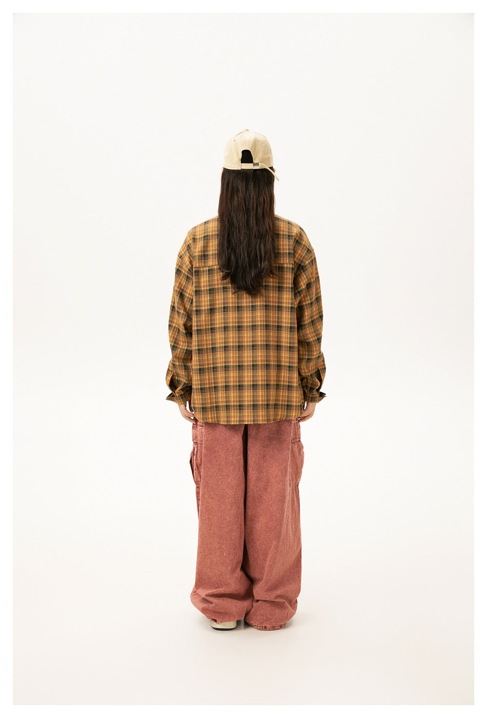 Rear view of a model wearing a mustard yellow plaid shirt and loose rose-colored pants.