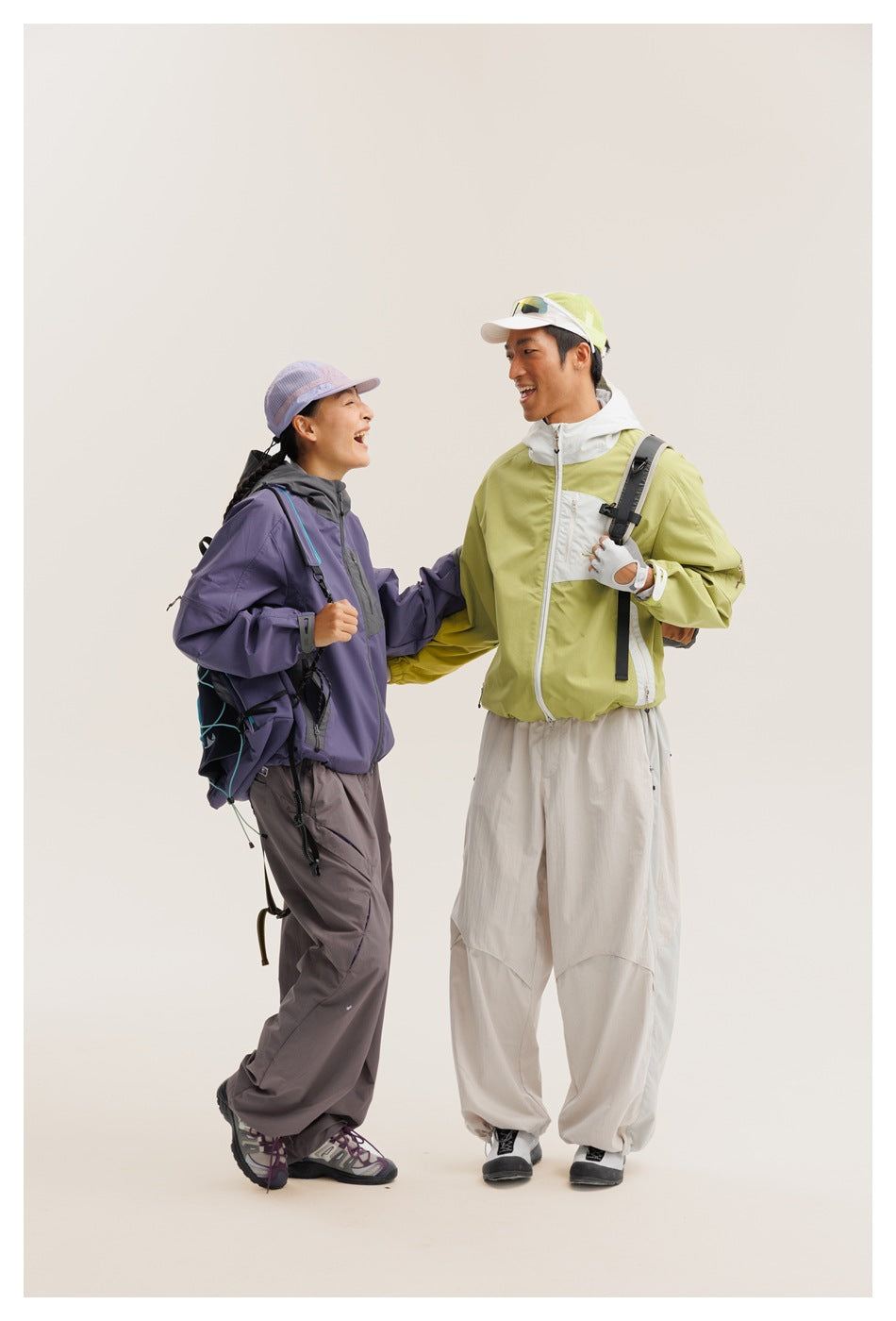 Two models face each other wearing purple and charcoal, and lime-green and white outdoor jackets.