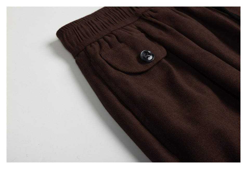 Close-up of a buttoned flap pocket and gathered elastic waistband on dark brown pants.