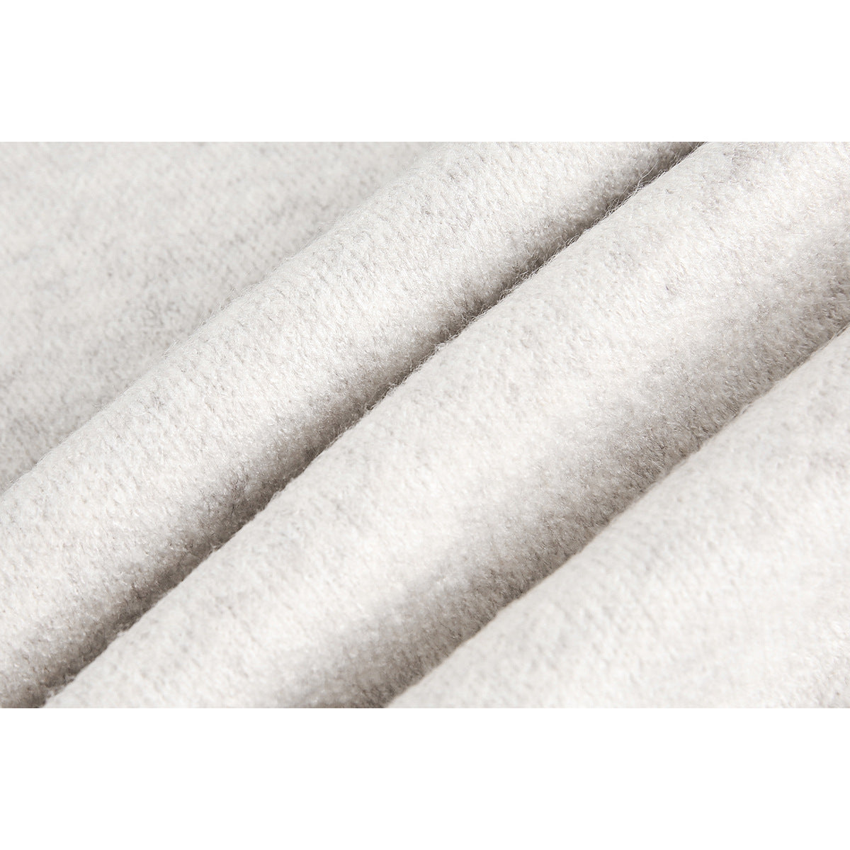 Close-up of ivory sweater knit folded into soft ridges, showing its fuzzy surface texture.