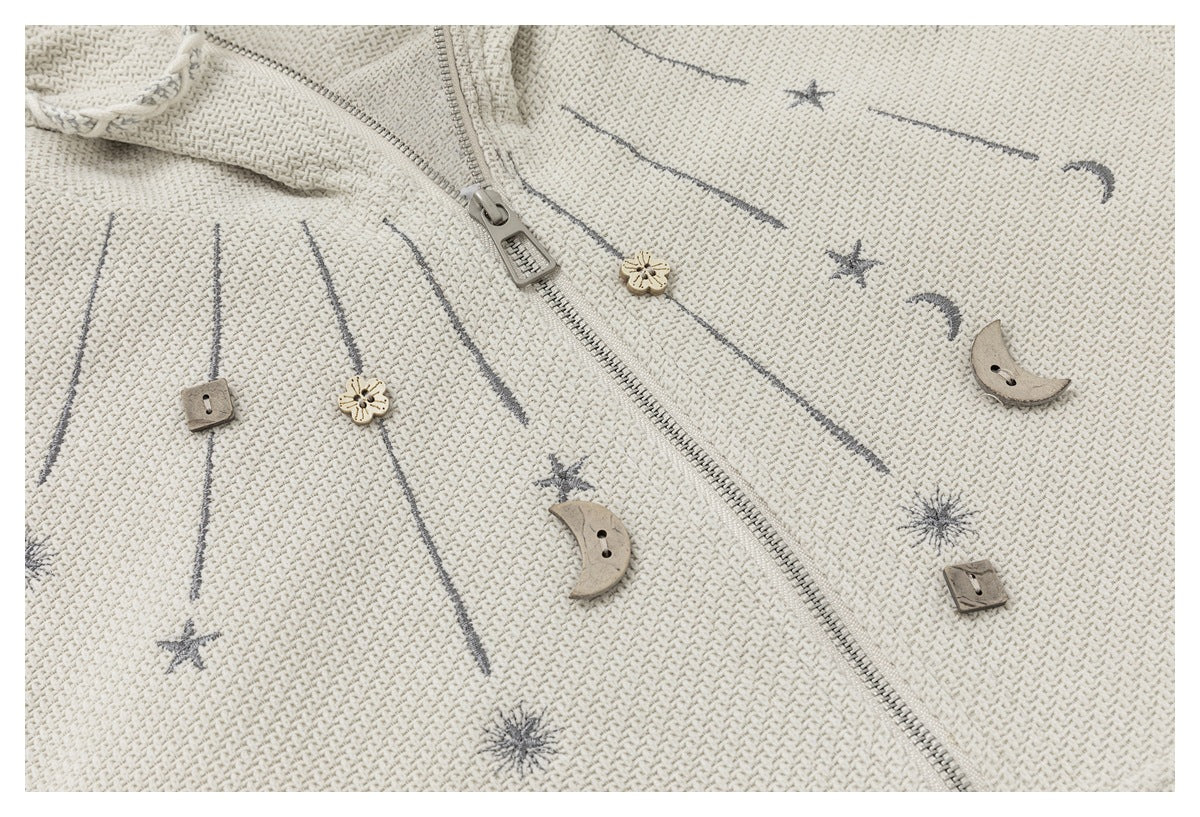 Close-up of gray stars, moons, and line motifs with decorative buttons on the ivory jacket.