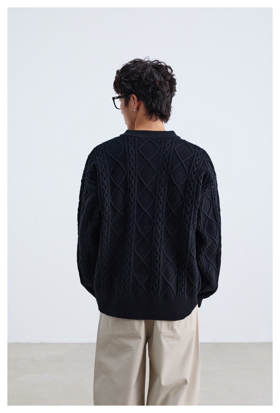 Back view of a model wearing a black cable-knit sweater with diamond patterns and ribbed trim.