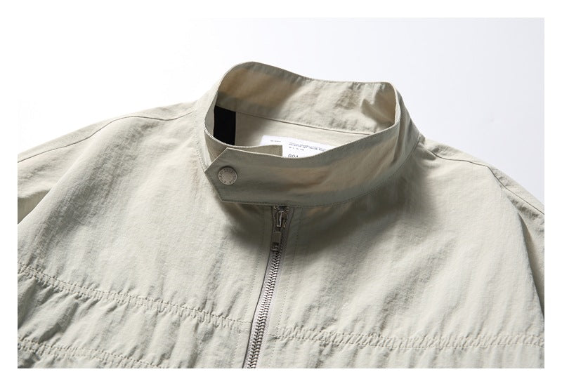 Close-up of a light stone-gray jacket’s stand collar, snap tab, and central zipper.