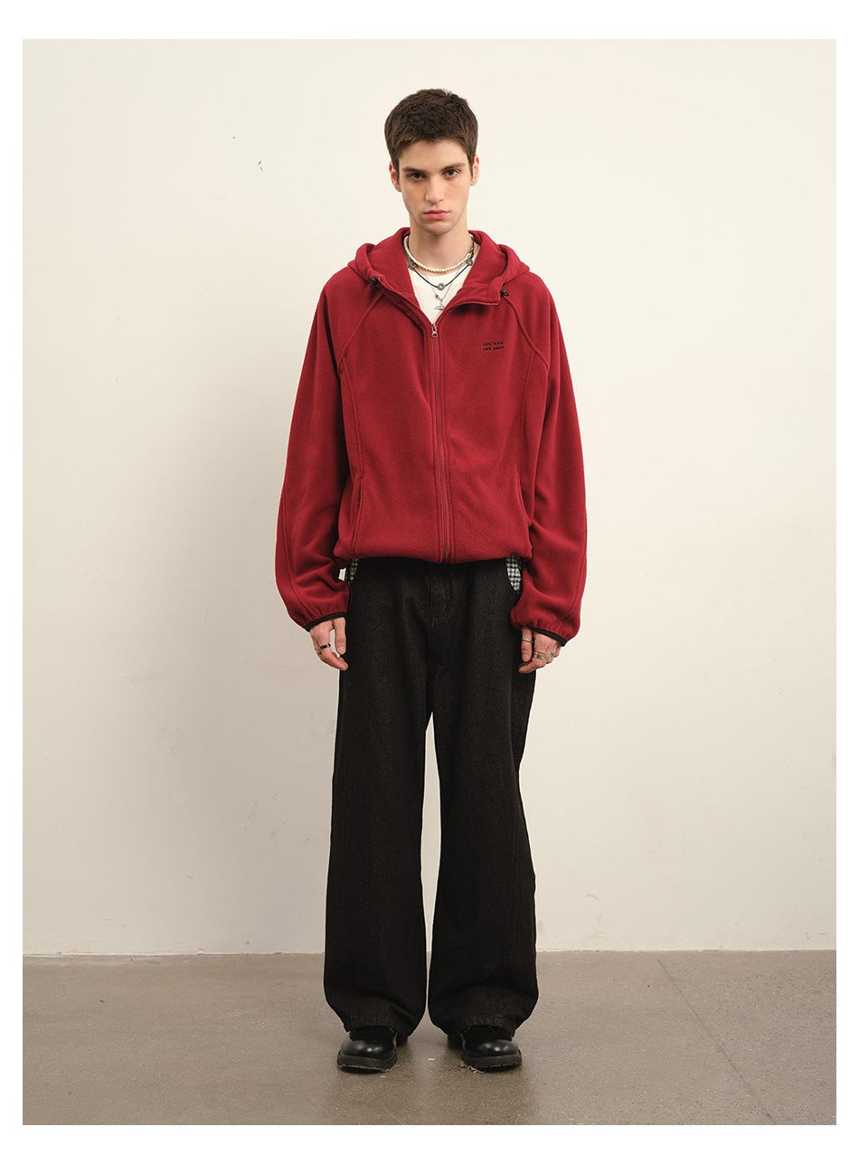 Full-length front view of a man wearing a red hooded zip jacket with small dark chest lettering and black wide-leg pants.