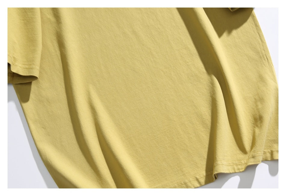 Close-up of a plain pale yellow T-shirt front and lower hem laid flat.