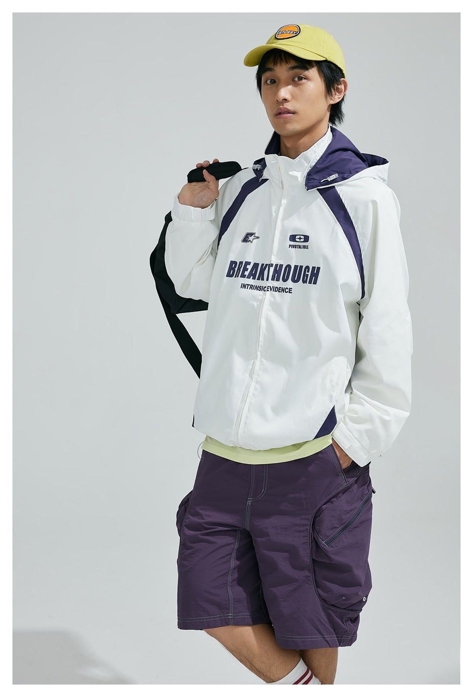Model in white hooded jacket with purple accents holding a bag over the shoulder, three-quarter view