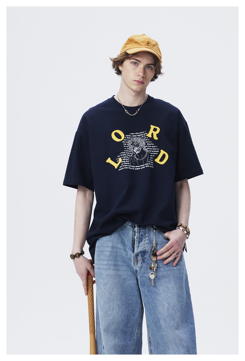 Close view of a model wearing a navy T-shirt with a yellow-lettered graphic and a mustard cap.