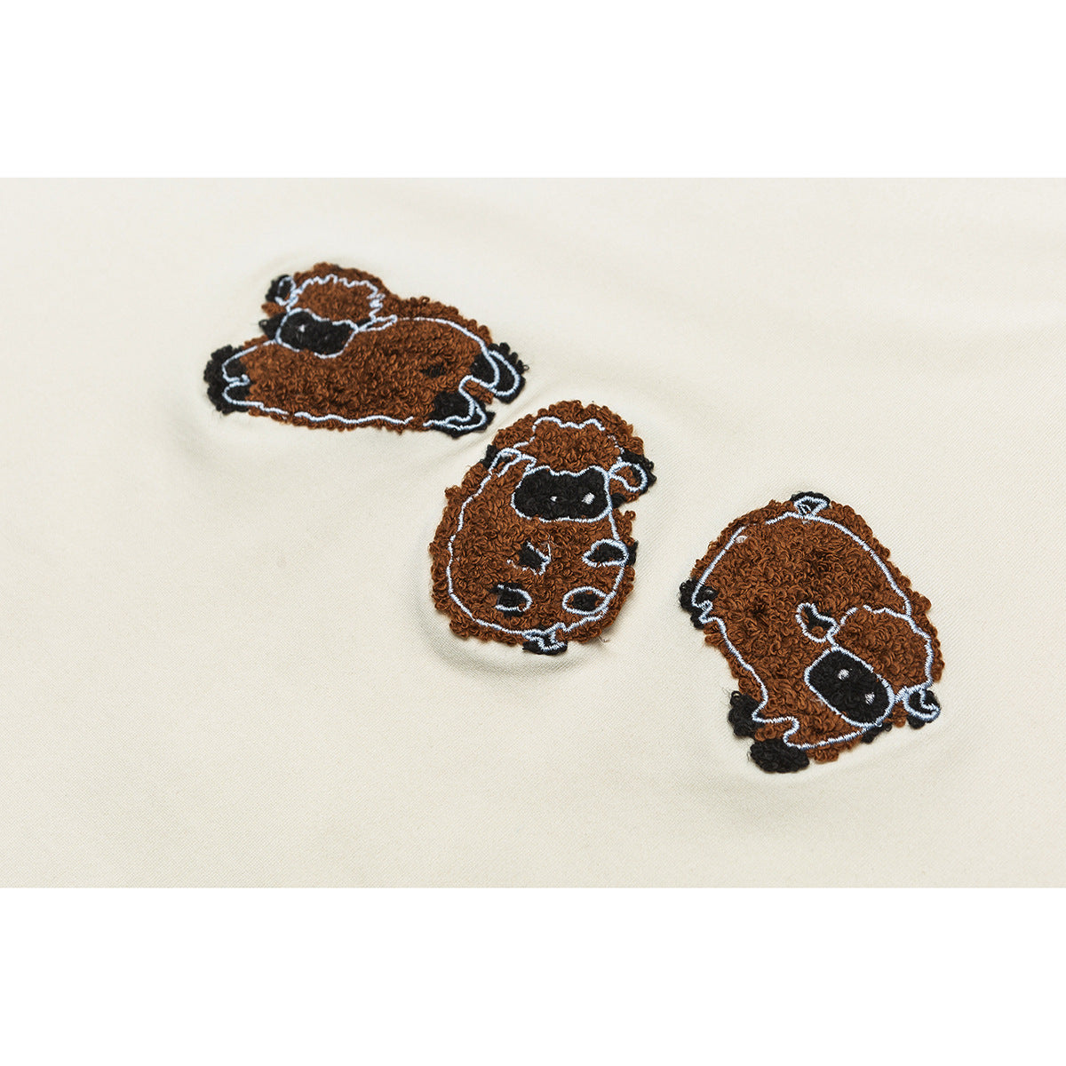 Close-up of three brown sheep embroidered on ivory sweatshirt fabric.