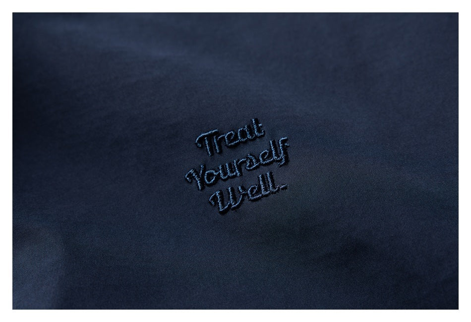 Close-up of navy fabric with dark embroidered text reading “Treat Yourself Well.”