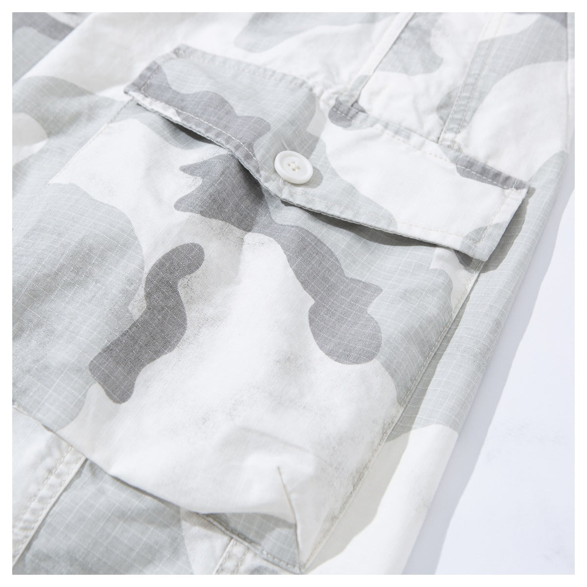 Close-up of a buttoned flap pocket on light gray and white camouflage shorts.