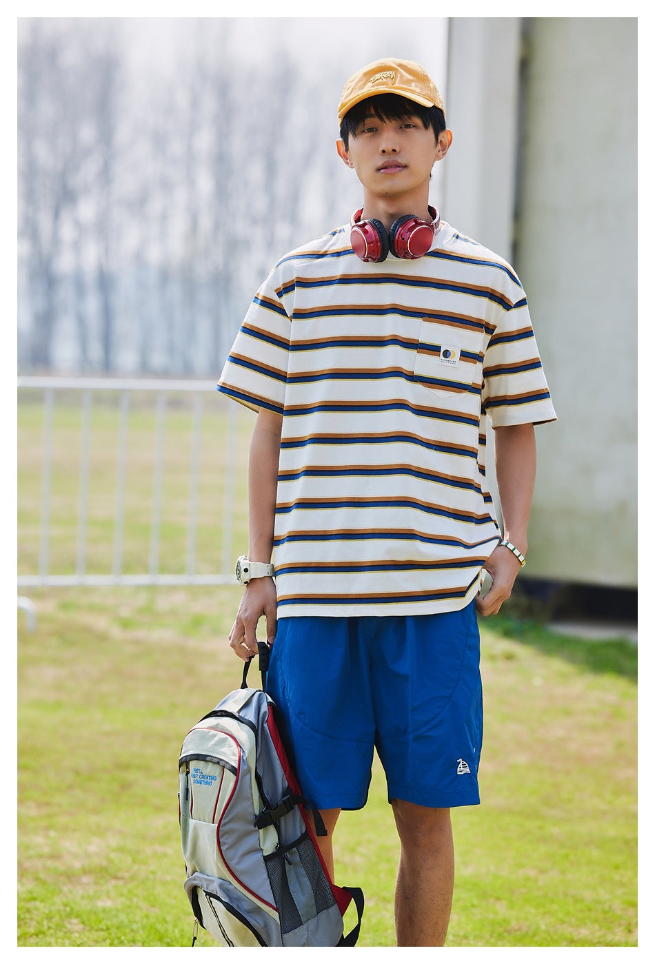 Man facing forward in a white striped pocket T-shirt and bright blue shorts outdoors.