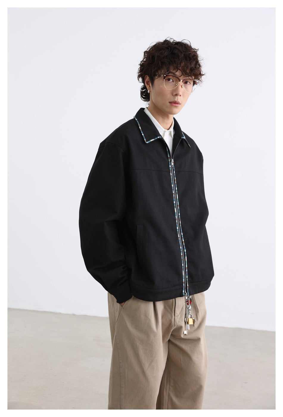 Model wearing a black zip-front jacket with multicolor trim, white shirt and khaki trousers, angled view