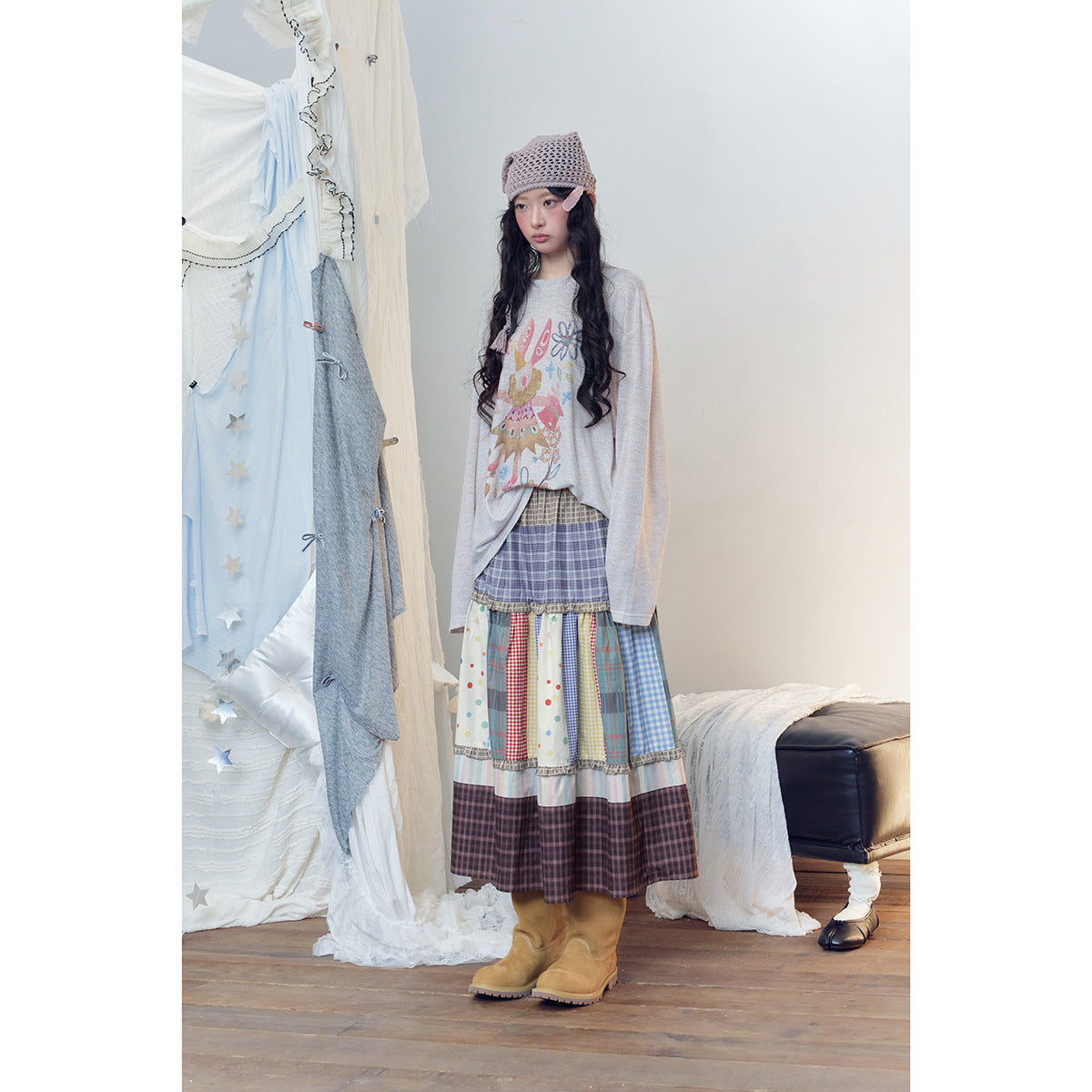 Model wearing a gray graphic top and a long tiered skirt with colorful mixed plaid, gingham, polka-dot, and striped panels.