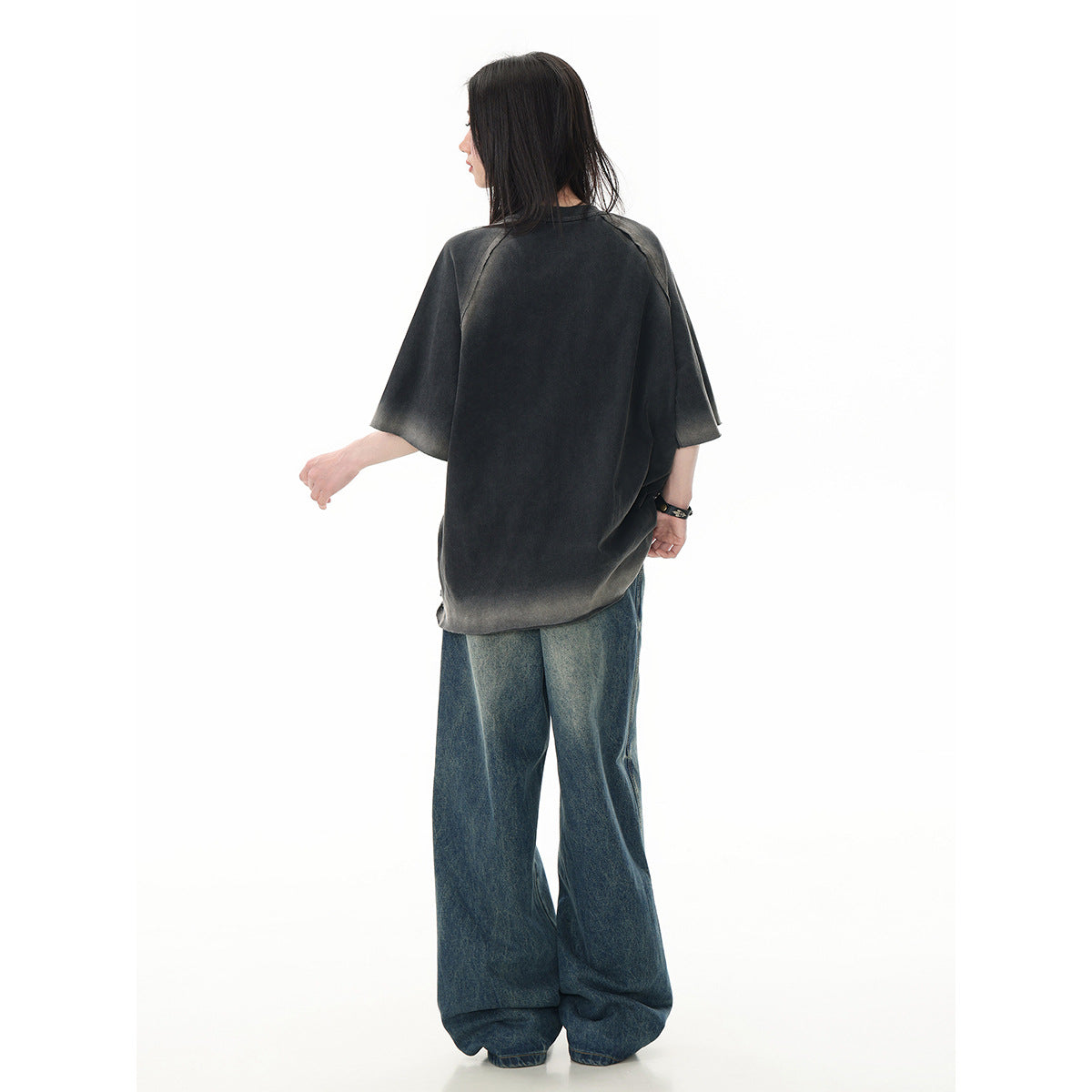 Rear view of a model wearing an oversized charcoal T-shirt and wide-leg blue jeans.
