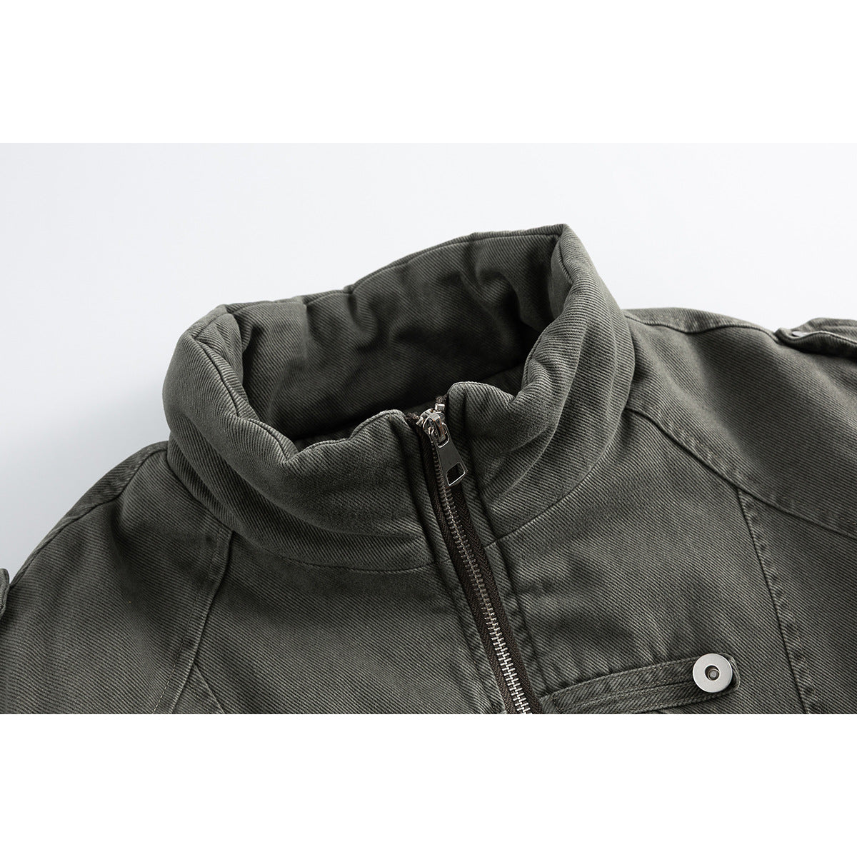 Close-up of a charcoal gray jacket's high collar, front zipper, and a buttoned chest strap.