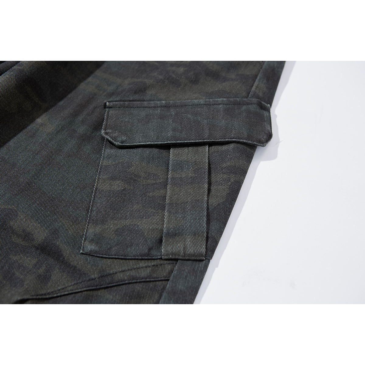 Close-up of a flap cargo pocket and stitching on dark charcoal camouflage pants.