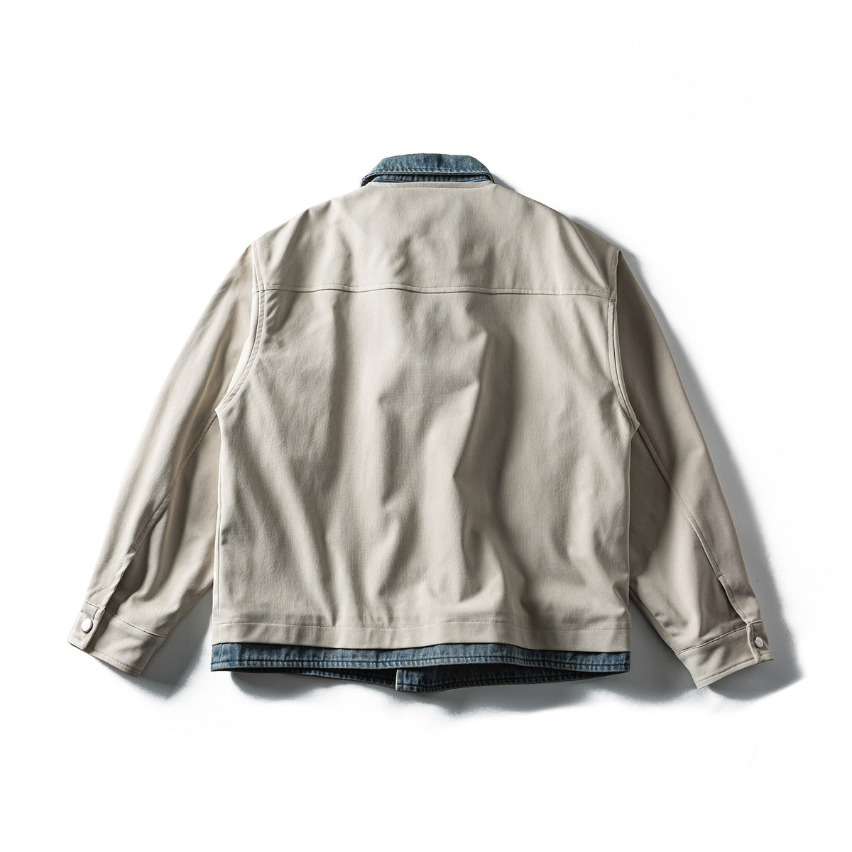 Back view of a beige jacket with blue denim accents at the collar and hem, laid flat.