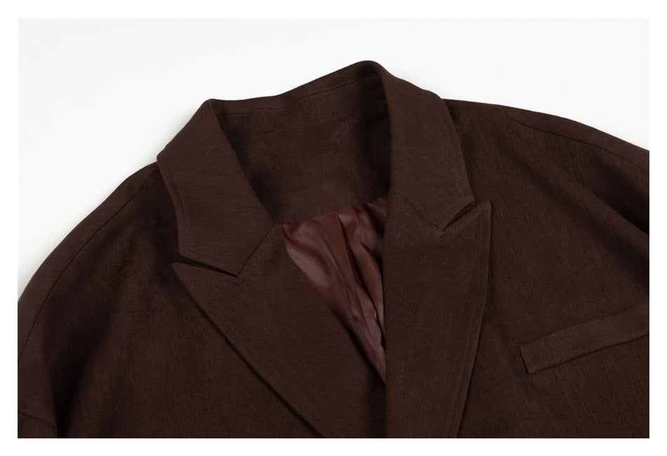 Close-up of a dark brown blazer showing its notched lapels, burgundy lining, and chest welt pocket.