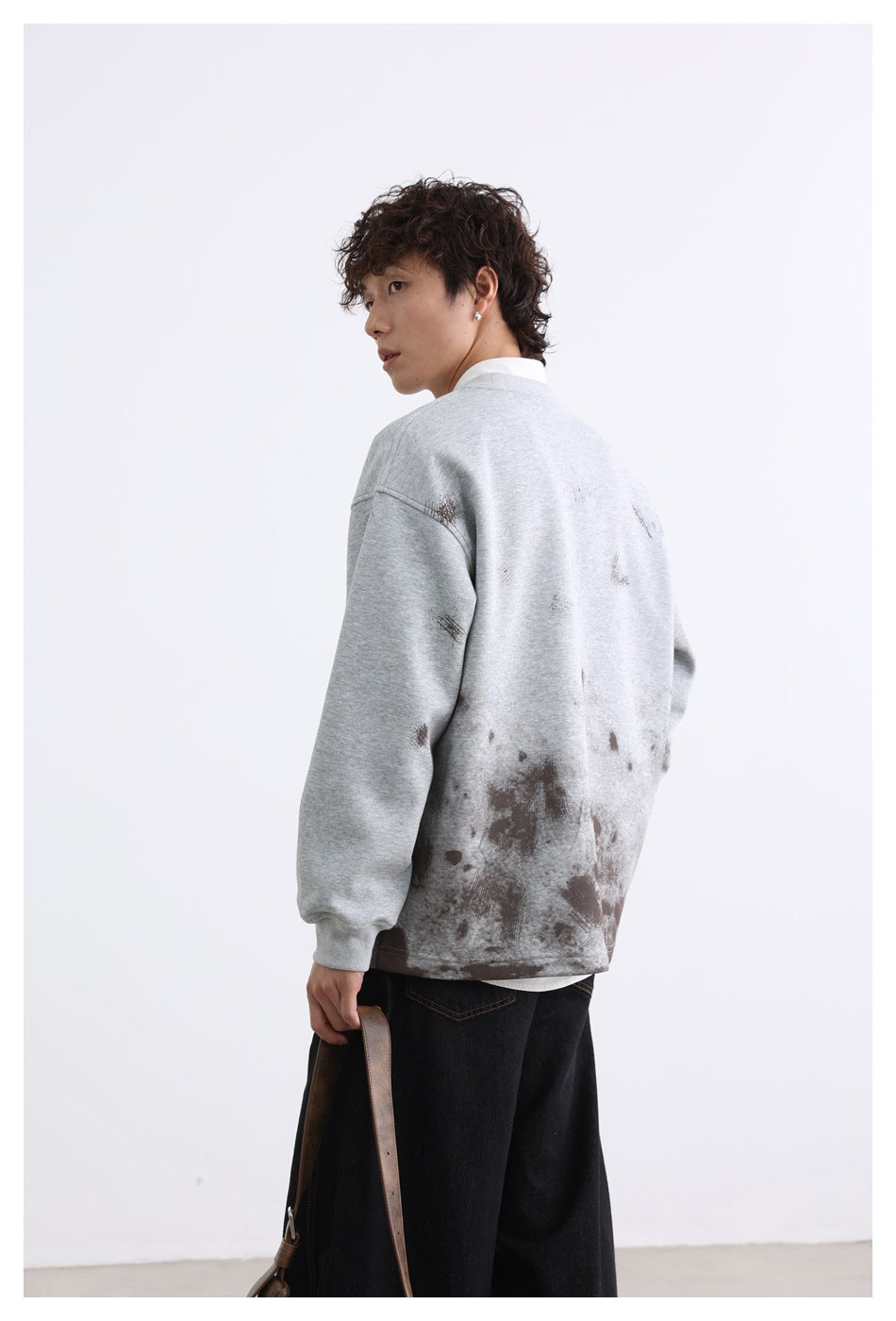 Rear three-quarter view of a model wearing a light gray sweatshirt with dark distressed marks across the back and hem.