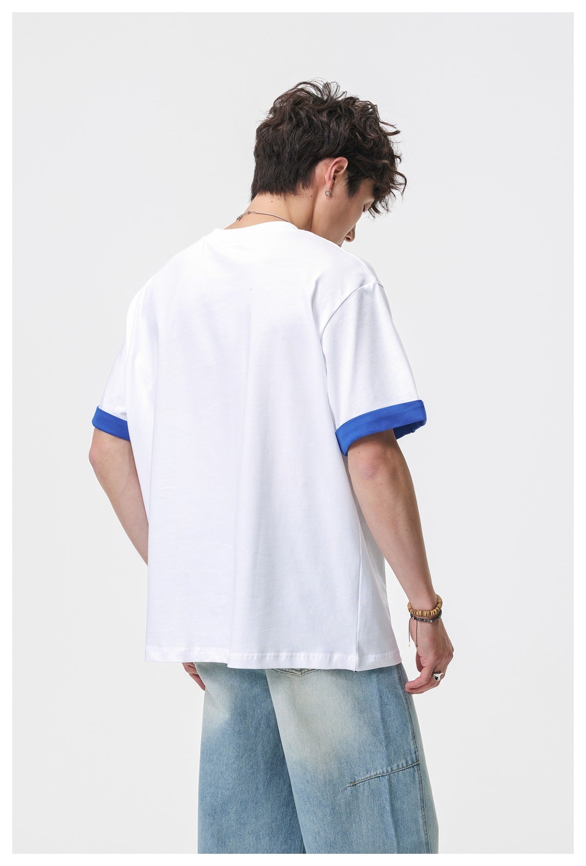 Model wearing a white short-sleeve T-shirt with blue rolled cuffs, shown from the back.