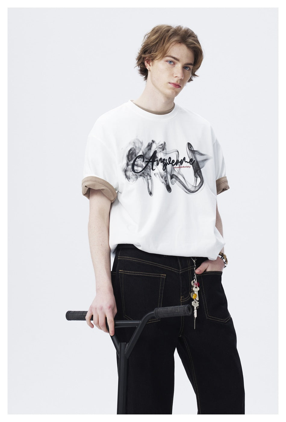 Close view of a model wearing a white graphic T-shirt with tan rolled cuffs and loose black trousers.