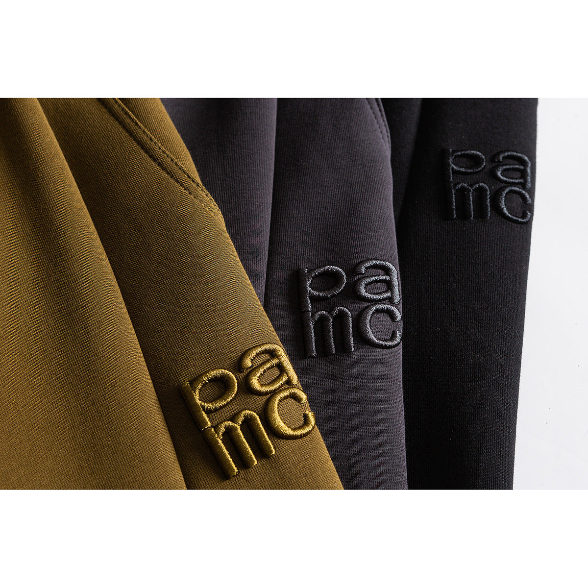 Close-up of mustard, charcoal, and black pants with raised tonal lettering embroidered on the legs.