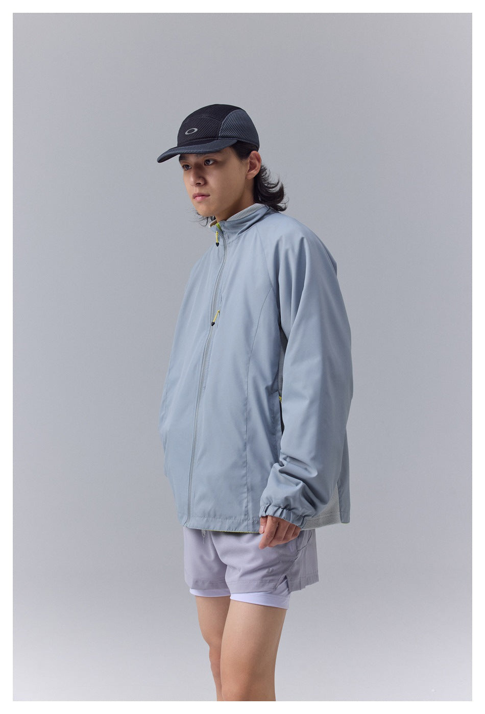 Model wearing a pale blue-gray zip jacket with gray shorts, shown from the front at a slight angle.