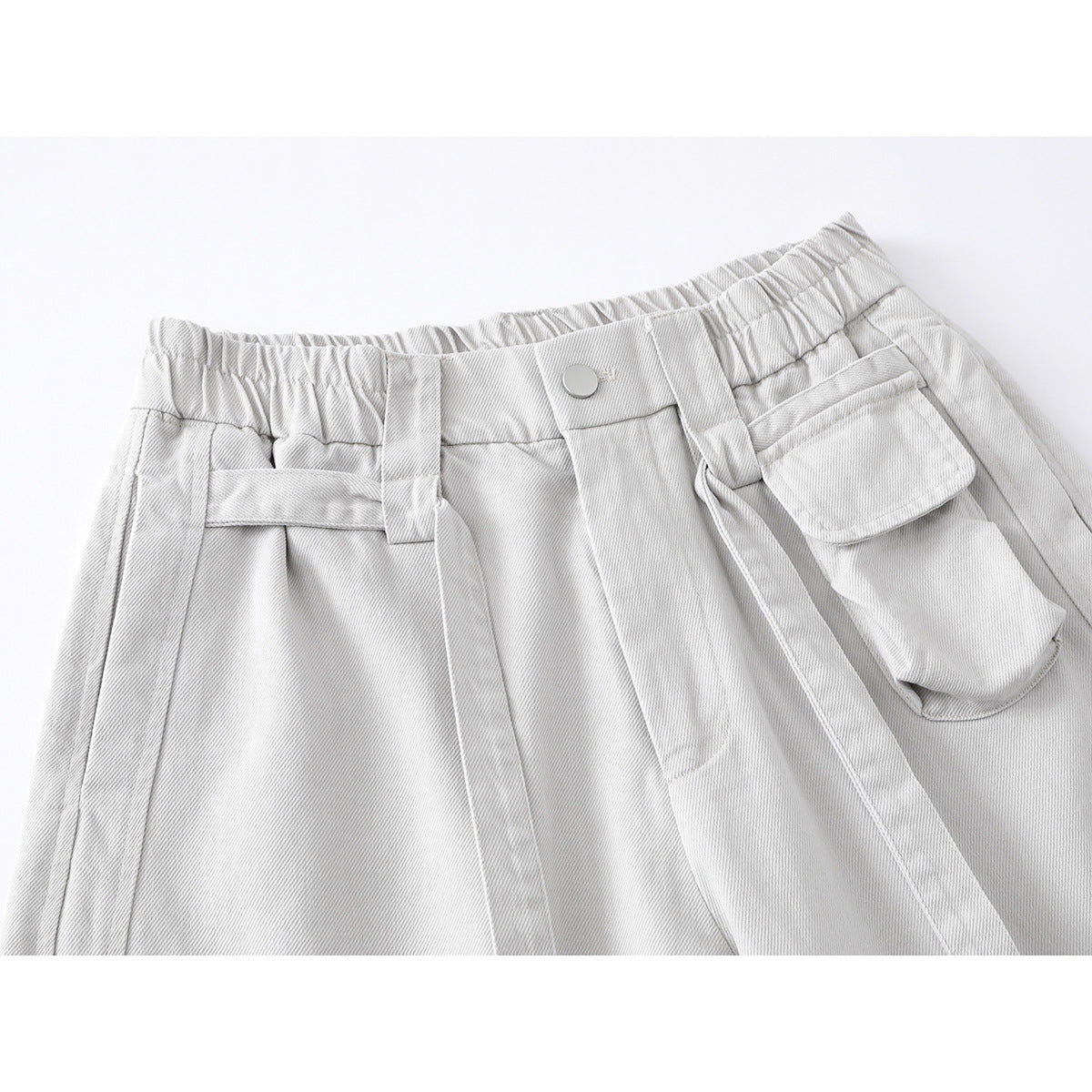 Close-up of light gray cargo trousers showing an elastic waistband, button closure, belt loops, and flap pocket.