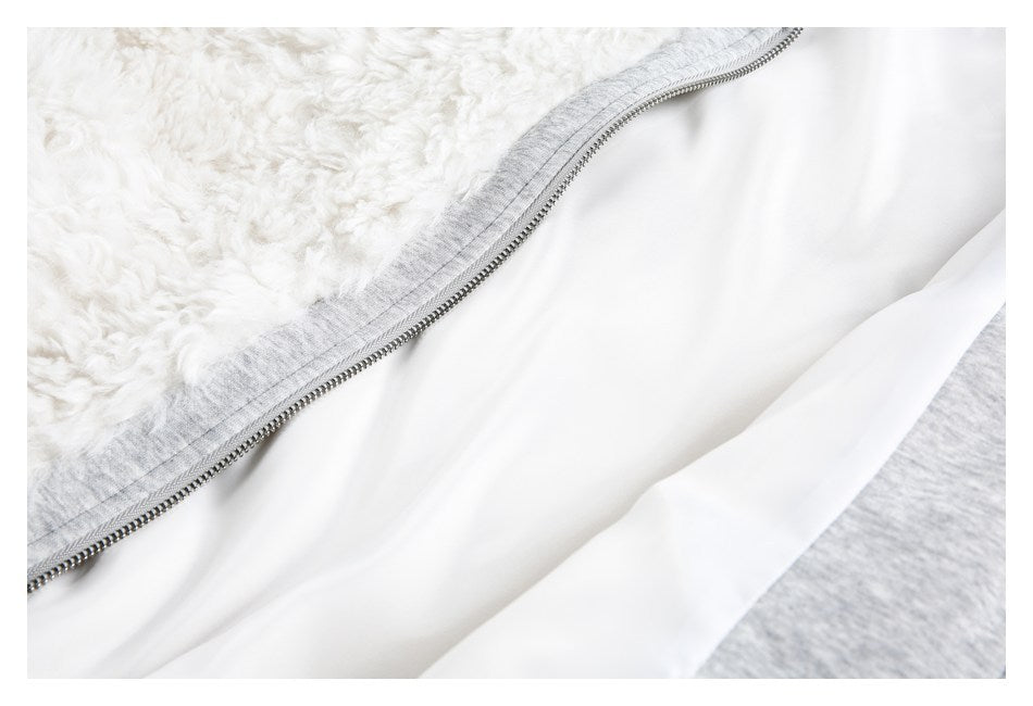 Close-up of a metal zipper joining white shaggy trim to a smooth white lining and gray fabric.